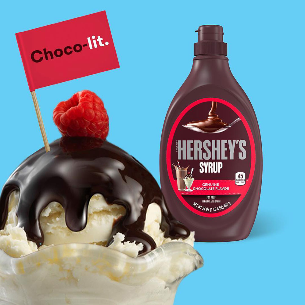 A bottle of Hershey's chocolate syrup sits behind a fudged up ice cream sundae which has a red flag in it reading 'Choco-lit'.