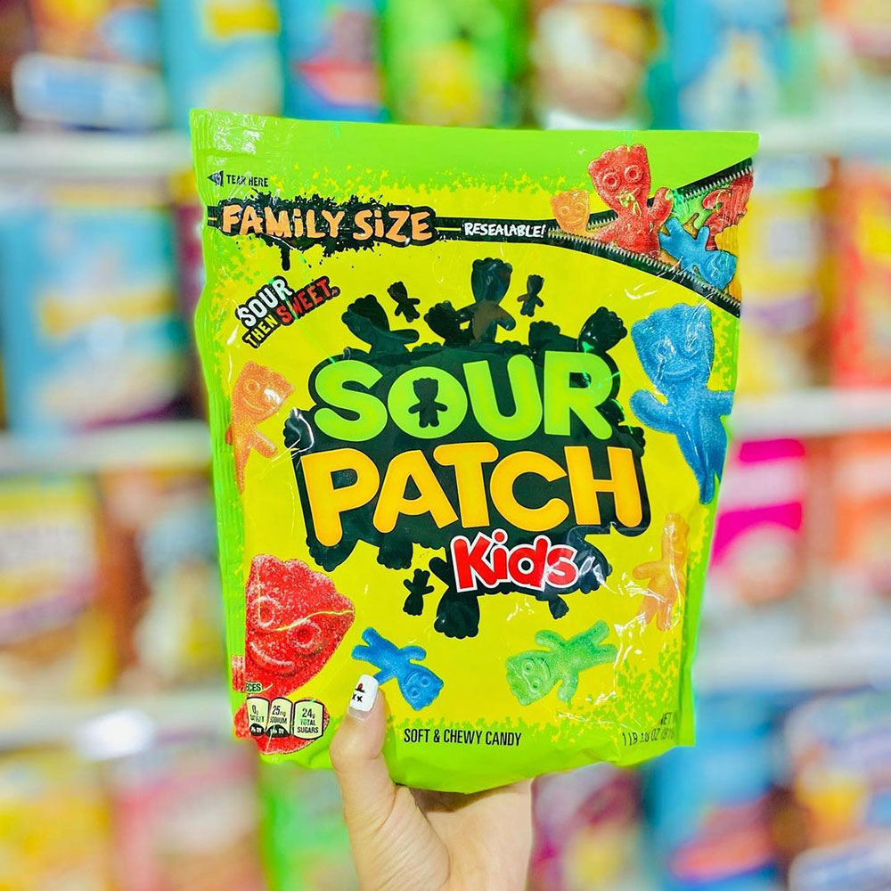 A hand holds up a packet of Sour Patch Kids at the supermarket.