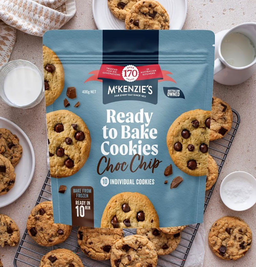 Overhead view of cookies on a baking tray, covered with an image if a pack of McKenzie's Ready to Bake Cookies.